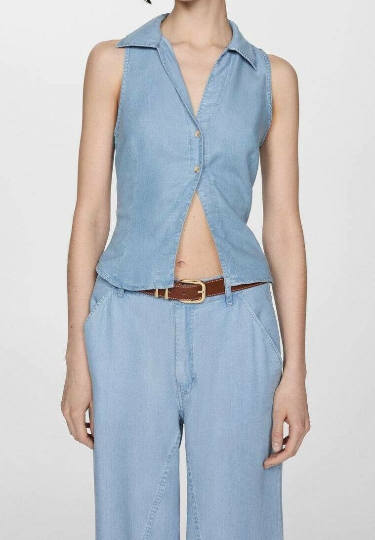 Chemise sans manches en denim bleu clair avec col et boutons, associée à un pantalon ample assorti et une ceinture marron.