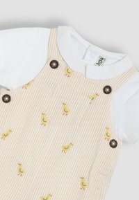 Lichtgekleurde gestreepte tuinbroeken met gele eendpatronen en donkere knoopaccenten, gecombineerd met een witte blouse eronder.
