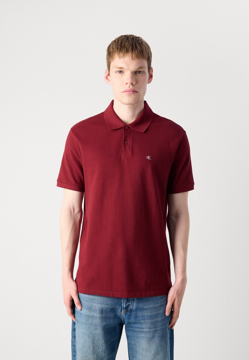 Bordowa koszulka polo z klasycznym kołnierzykiem i krótkimi rękawami; posiada małe logo na lewej piersi; materiał bawełniany; gładka faktura.