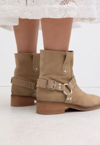 Hellbraune Wildleder-Stiefeletten mit abgerundetem Zeh, seitlicher Schnalle und silbernen Beschlägen. Verfügen über einen Holzabsatz und eine weiche Textur.