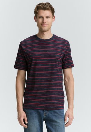 Kurzes Herren-T-Shirt in Marineblau mit roten Streifen. Aus Baumwollmaterial, Rundhalsausschnitt, lockere Passform. Getragen mit hellblauen Jeans.