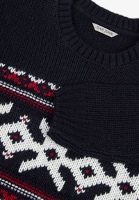 Ciemnobłękitny sweter z dzianiny z czerwonymi, białymi i czarnymi wzorami geometrycznymi. Żebrowany dekolt w kształcie łódki i mankiety, o miękkiej strukturze.