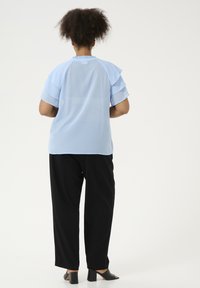 Light blue shirt with layered ruffle sleeves, rounded neckline, paired with black wide-leg pants and black heeled mules.