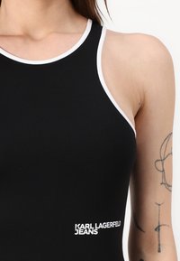 Bodysuit sin mangas negro con ribete blanco, con un logo que dice "KARL LAGERFELD JEANS" en el lateral. Tela suave y diseño ajustado.