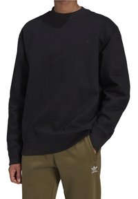Svart crewneck-tröja med ribbad halsringning och ärmslut, med en liten pr präglad logotyp på bröstet. Tillsammans med olivgröna sweatpants.