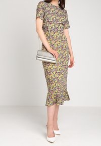 Kwiatowa sukienka midi z krótkim rękawem, z żółto-różowym wzorem, rozkloszowanym dołem, zestawiona ze srebrną kopertówką i białymi szpilkami.