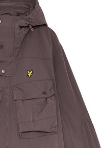 Vattentålig lila jacka med huva, med ojämn textur, tryckknappar och två stora framfickor. Gul logotyp på bröstet.