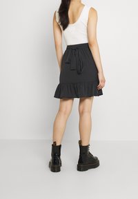 Jupe noire à volants avec un lien à la taille, fabriquée en tissu doux. Associée à des bottes de combat noires épaisses. Texture lisse et design évasé.