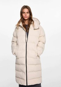 Cappotto puffer beige con cappuccio, dotato di zip frontale, design trapuntato e polsini elasticizzati. Texture liscia con vestibilità comoda.