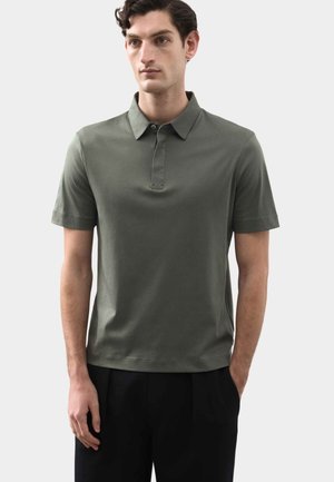 Koszulka polo z krótkim rękawem w oliwkowym zielonym kolorze, wykonana z miękkiej tkaniny. Posiada klasyczny kołnierzyk oraz listwę z guzikami. Prosty, schludny design.