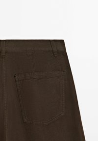 Pantaloni verde scuro con vita, dotati di una tasca posteriore singola. Il tessuto sembra resistente con una texture liscia.