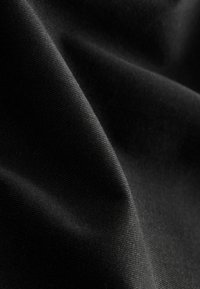 Gros plan d'un tissu noir lisse avec une texture de tissage fine visible et des plis doux créant des contrastes de lumière et d'ombre.