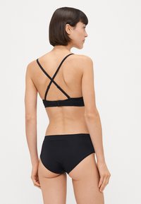 Completo da bagno nero con design incrociato sulla schiena, tessuto morbido e slip a vita media. Il materiale è liscio e dallo stile minimalista.