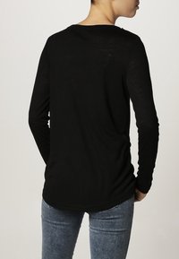 Czarna bluzka z długim rękawem wykonana z lekkiego, teksturowanego materiału, z okrągłym dekoltem i zakrzywionym dołem, zestawiona z jasnymi dżinsami.