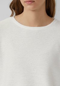 Witte textuur top met horizontale ribbels, met een klassieke ronde halslijn en zachte stof, die tot aan het sleutelbeen reikt.