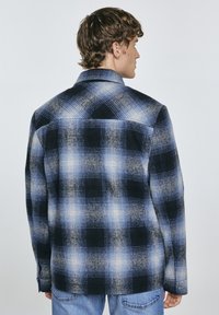 Camicia in flanella a quadri blu e nera con maniche lunghe e polsini abbottonati, caratterizzata da una texture morbida e una vestibilità leggermente rilassata.