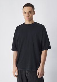 Zwarte oversized katoenen t-shirt met korte mouwen, ronde halslijn en zichtbaar merklogo op de linker mouw. Casual fit en eenvoudig ontwerp.