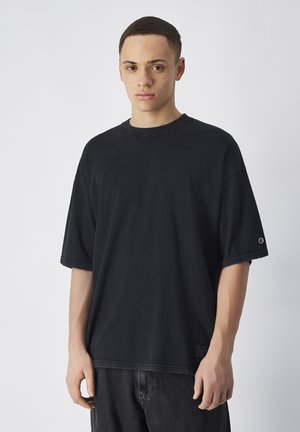 Czarna, oversized bawełniana koszulka z krótkim rękawem, okrągłym dekoltem i widocznym logo marki na lewym rękawie. Swobodny krój i prosty design.
