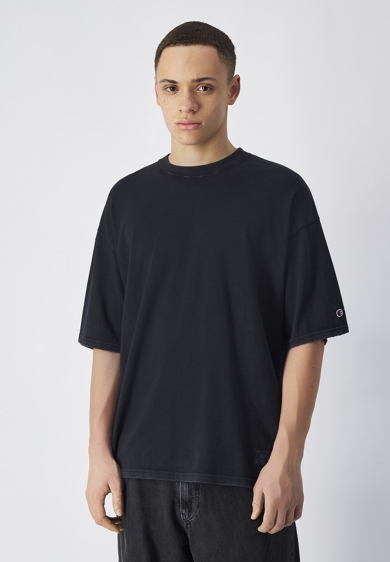 Zwarte oversized katoenen t-shirt met korte mouwen, ronde halslijn en zichtbaar merklogo op de linker mouw. Casual fit en eenvoudig ontwerp.