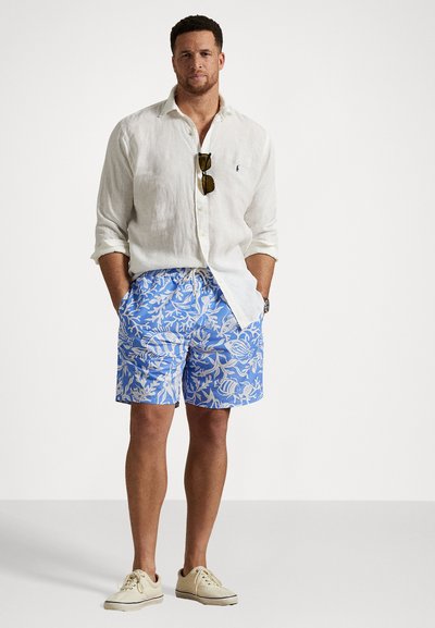 Linenová košeľa s gombíkmi, biela; modré plavky s bielym kvetinovým a rybím vzorom; svetlé tenisky. Jednoduchý a neformálny letný outfit.