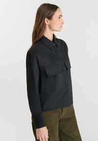 Black button-up shirt featuring two chest pockets, a collar, and long sleeves. The fabric has a subtle texture and a loose fit.