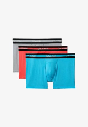 Trois paires de boxers homme en bleu, rouge et gris avec des ceintures noires arborant le logo Calvin Klein dans des couleurs contrastantes.