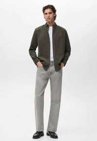 Camisa verde oliva de botones sobre una camiseta blanca, combinada con jeans grises y zapatos negros. Diseño sencillo con cortes clásicos.