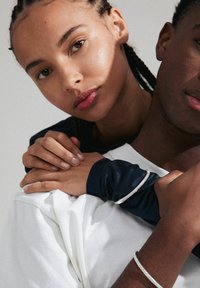 Une paire d'individus, l'un en t-shirt blanc, l'autre en haut à manches longues bleu marine, mettant en avant des textures lisses et un design minimaliste.