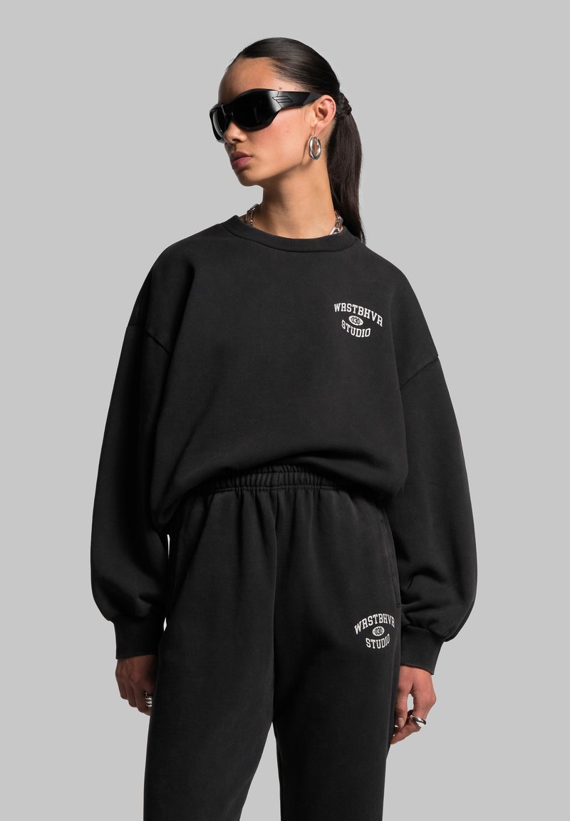 Schwarzes Sweatshirt- und Hosen-Set aus weichem Stoff. Das Sweatshirt hat überschnittene Schultern und ein Logo-Detail. Die Hose verfügt über einen elastischen Bund.