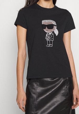 Schwarzes T-Shirt mit einer Cartoon-Figur aus Strasssteinen, die eine Sonnenbrille und einen Anzug trägt, kombiniert mit einem schwarzen Lederminirock.