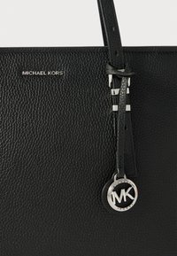 Fekete textúrált bőrtáska ezüst hardware-rel. Leválasztható pánttal és kör alakú MK logóval díszítve. "MICHAEL KORS" felírat a fronthal.