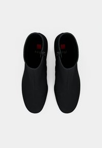 Botas de tornozelo pretas com uma textura suave, apresentando um design elegante, bico arredondado e detalhes de fecho zip discreto nas laterais.