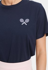 Navy cotton t-shirt with short sleeves and a round neckline. Features white embroidered tennis rackets on the left chest area.