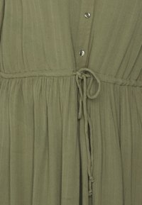 Olivgrön klänning med texturerad bomull, har knäppning framtill, elastiskt midjeband och justerbar snöre med en rynkad kjol.
