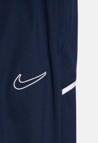 Tamsiai mėlynos sportinės šortai iš kvėpuojančios medžiagos, su balta Nike logotipu ir baltu šoniniu dryžiu. Tekstūruota ir lygi apdaila.