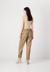 Beige tanktop gecombineerd met lichtbruine neplederen broek met een elastische tailleband, twee achterzakken en een zwart logo-detail op de zoom.