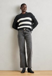 Svart og hvit rutete strikkegenser med sideskatter, kombinert med høy midje svarte jeans og ankelstøvler. Glatt tekstur, avslappet passform.
