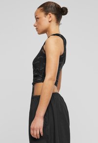 Svart cropped tank topp med et gjentakende "KARL" logo-mønster, laget av et mykt stoff; kombinert med løs passform svarte bukser.