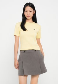 Żółta koszulka z krótkim rękawem z małym logo na klatce piersiowej, w połączeniu z szarym plisowanym spódnicą z dwoma guzikami.