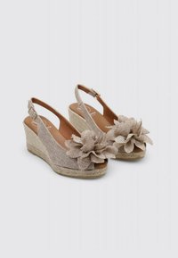 Sandales à talon compensé beiges avec une tige en tissu tissé, accent floral, bout ouvert et plateforme en corde texturée. Fermeture à boucle au talon.