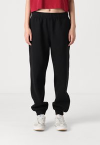 Zwarte trainingsbroek met een elastische tailleband, losse pasvorm en geribbelde boorden. Gepaard met grijze en witte sneakers.