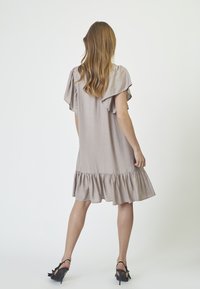 Beige, polven pituinen mekko, jossa on lepattelevat hihat ja röyhelöhelma. Silkkinen pinta, kevyt materiaali; yhdistetty mustiin korollisiin kenkiin.