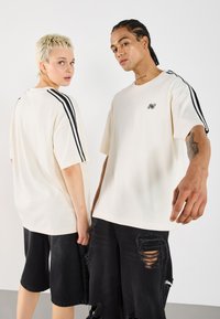 T-shirts oversize crème avec des rayures noires sur les côtés, manches courtes et un petit logo sur la poitrine ; associés à des shorts en denim noir déchirés.