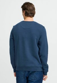 Mornarskoplavi dukserica napravljena od mekog materijala, sa dugim rukavima, okruglim izrezom i rebrastim manžetama i donjim rubom. Glatka tekstura s minimalnim dizajnom.