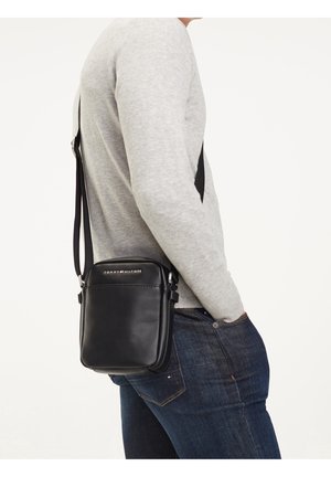 Musta nahkainen olkalaukku suorakaiteen muotoinen, varustettu hopeisilla metalliosilla ja logolapulla. Säädettävä olkahihna kiinnitetty.