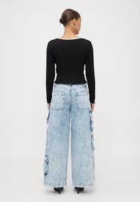 Black long-sleeve top with a scalloped hem paired with light-wash wide-leg cargo jeans featuring multiple pockets and an elastic waistband.