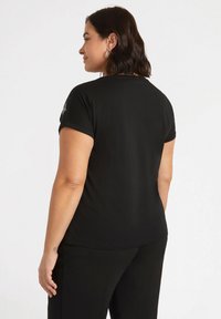 Camiseta negra de manga corta en una tela suave y elástica. Diseño simple con cuello redondo y un ajuste ligeramente holgado.