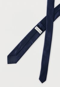 Cravate en soie bleu marine avec une texture lisse et une pointe pointue. L'étiquette portant la mention "PIER ONE" est située près de l'extrémité étroite de la cravate.
