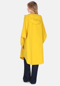 Pelerină de ploaie galbenă impermeabilă, cu glugă, design supradimensionat, nasturi capse și mâneci lungi. Purtați peste blugi albastru închis și adidași.