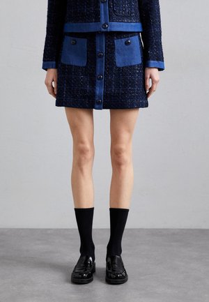 Marineblaues Tweed-Jacket- und Rock-Set mit blauen Akzent-Taschen und Knopfverschluss. Kombiniert mit schwarzen gerippten Socken und Mokassins.